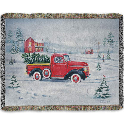 Woven blanket with a red truck and christmas tree design on a snowy background.