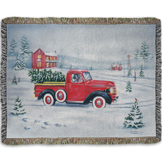 Woven blanket with a red truck and christmas tree design on a snowy background.