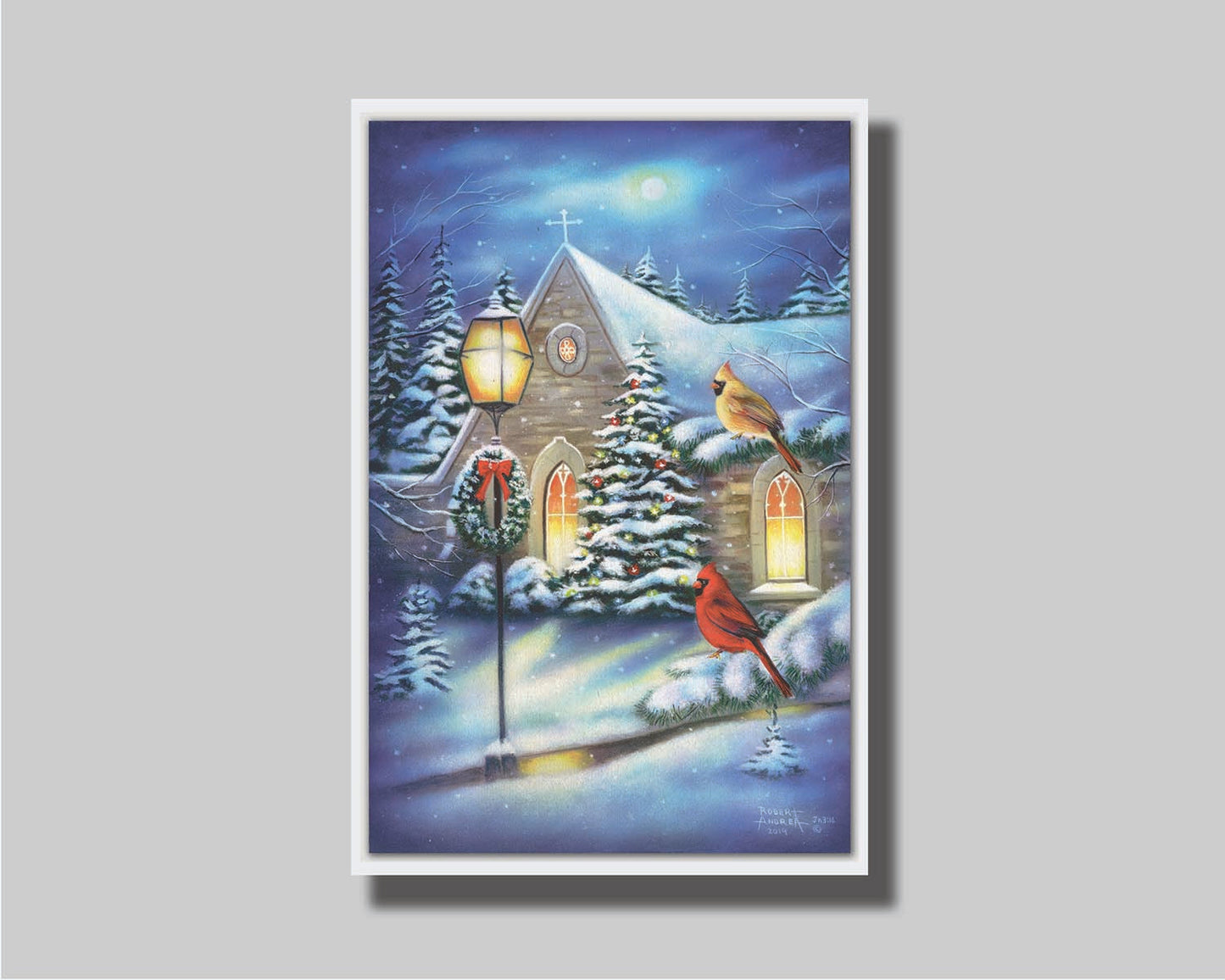 A painting of cardinals perched on evergreen branches on a snowy night, in front of a church decorated for Christmas. Printed on canvas in a float frame.