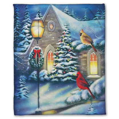 Coral fleece blanket designed with a snowy christmas scene in a church courtyard, where cardinals are perched on evergreen tree branches.