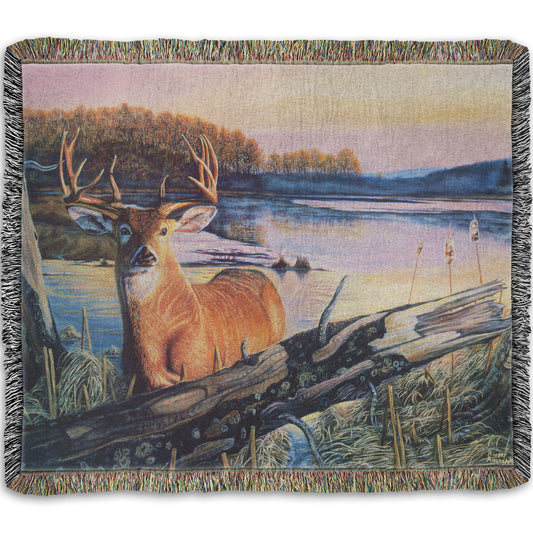 Woven throw blanket designed with a painting of a deer in front of a lake reflecting the morning sky.
