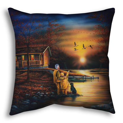 A throw pillow designed with a painting of a man and a child standing by a river and cabin. They are watching geese fly overhead at sunset.