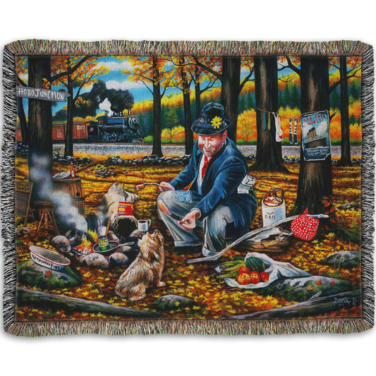 A woven throw blanket designed after a painting of a man sitting on a log at a campfire in the woods strewn with fall leaves. He is feeding a little dog. A train is passing in the background.