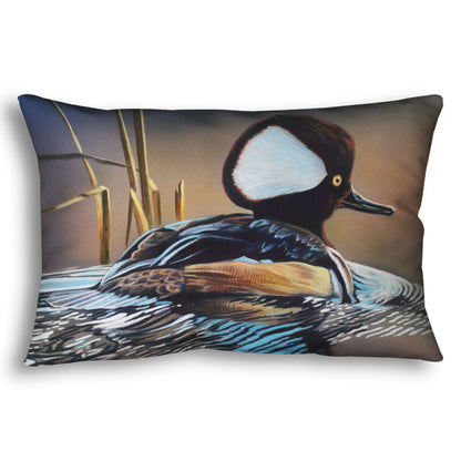 A throw pillow decorated with the design of a hooded merganser duck, floating on the water with its reflection rippling below.
