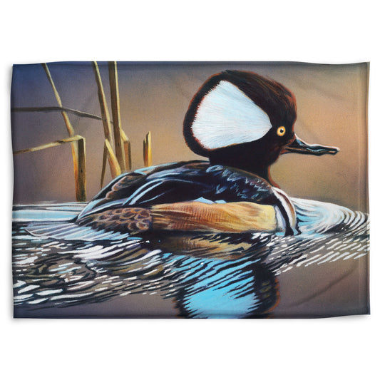 A coral fleece blanket decorated with the design of a hooded merganser duck, floating on the water with its reflection rippling below.