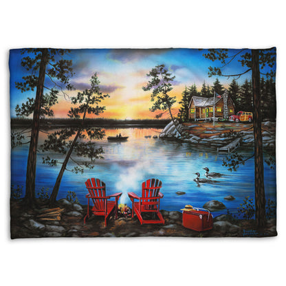 A coral fleece throw blanket designed after a painting of a lake at sunset, with a campfire in the foreground. Two loons drift across the water, as well as two fishers.