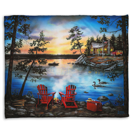A coral fleece throw blanket designed after a painting of a lake at sunset, with a campfire in the foreground. Two loons drift across the water, as well as two fishers.