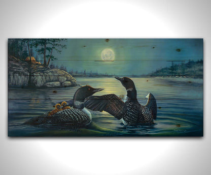 A painting of two grown loons, with two baby loons on one of their backs. They are floating on a lake under the moonlight, with a campground on the land in the distance. Printed on a wood pallet.