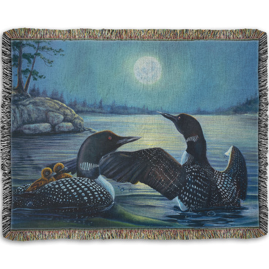 A woven throw blanket designed with a painting of two grown loons, with two baby loons on one of their backs. They are floating on a lake under the moonlight.