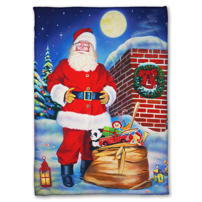 Festive blanket with a Santa Claus design. He stands on a snowy rooftop at night with a bag of toys.