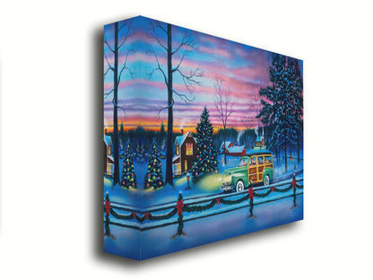 A painting of a snowy town, decorated with Christmas lights. A 1950s family drive past in a car full of presents at sunset. Printed on canvas.