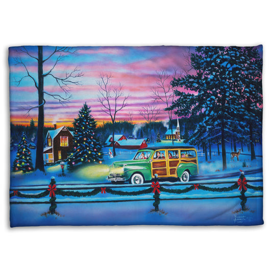 A coral fleece blanket printed with a painting of a snowy town with Christmas lights, where a 1950s family drive past in a car full of presents at sunset.
