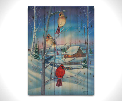 A painting of three cardinals, perched on branches above the snow. A cabin can be seen in the background, warm and inviting. Printed on a wood pallet.