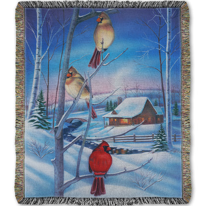 Woven throw blanket designed with a snowy winter scene, focused on cardinals near a cabin.