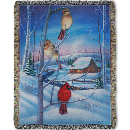 Woven throw blanket designed with a snowy winter scene, focused on cardinals near a cabin.
