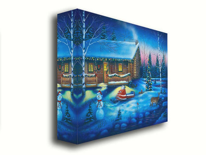 A painting of a snowy cabin decorated with Christmas lights. A deer treks through the snow in the yard, past a snowman to a stream. Printed on canvas.