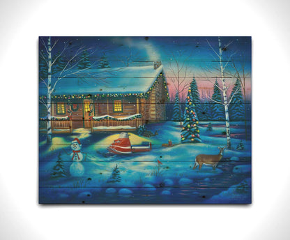 A painting of a snowy cabin decorated with Christmas lights. A deer treks through the snow in the yard, past a snowman to a stream. Printed on a wood pallet.