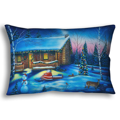 A festive throw pillow decorated with the painting of a snowy cabin decorated with Christmas lights.