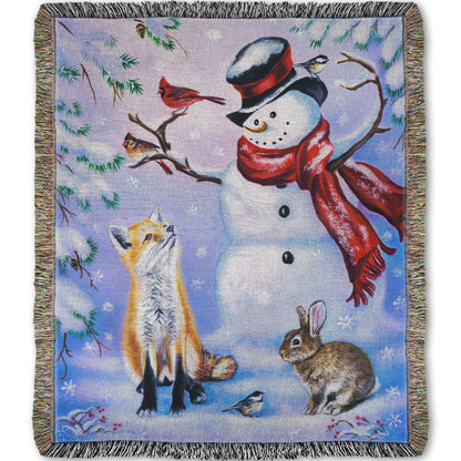 Woven blanket with a winter scene of a snowman, fox, cardinals, and rabbit around a snowman.