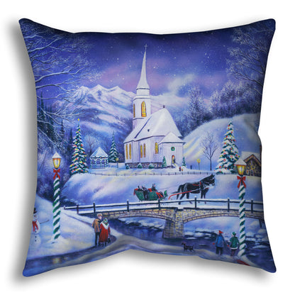 A throw pillow designed with a snowy mountain town, decorated for Christmas. A tall church sits in the middle of town.