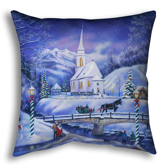 A throw pillow designed with a snowy mountain town, decorated for Christmas. A tall church sits in the middle of town.