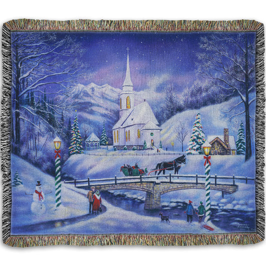 A woven throw blanket designed with a snowy mountain town, decorated for Christmas. A tall church sits in the middle of town.