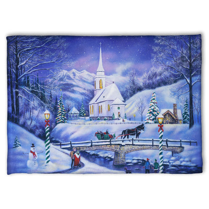 A coral fleece blanket designed with a snowy mountain town, decorated for Christmas. A tall church sits in the middle of town.
