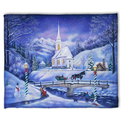 A coral fleece blanket designed with a snowy mountain town, decorated for Christmas. A tall church sits in the middle of town.