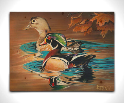 A painting of two wood ducks swimming through the water during fall. Their reflections are broken by the ripples of the water. Printed on a wood pallet.