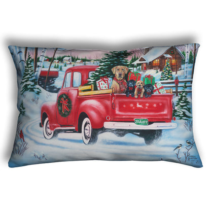 Festive throw pillow with a red truck carrying a Christmas tree, puppies, and presents in a snowy village scene.