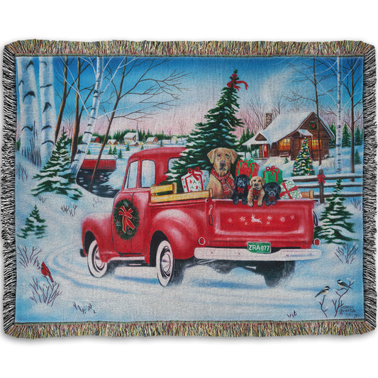 Festive woven blanket with a red truck carrying a Christmas tree, puppies, and presents in a snowy village scene.