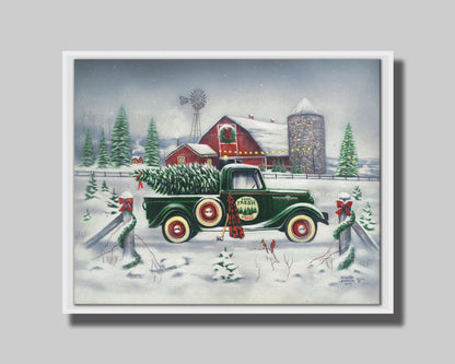 A painting of a green truck on a snowy road, preparing to deliver a freshly cut evergreen tree to a customer. A big red barn sits in the background, surrounded by large evergreens decorated for Christmas. Printed on canvas in a float frame.