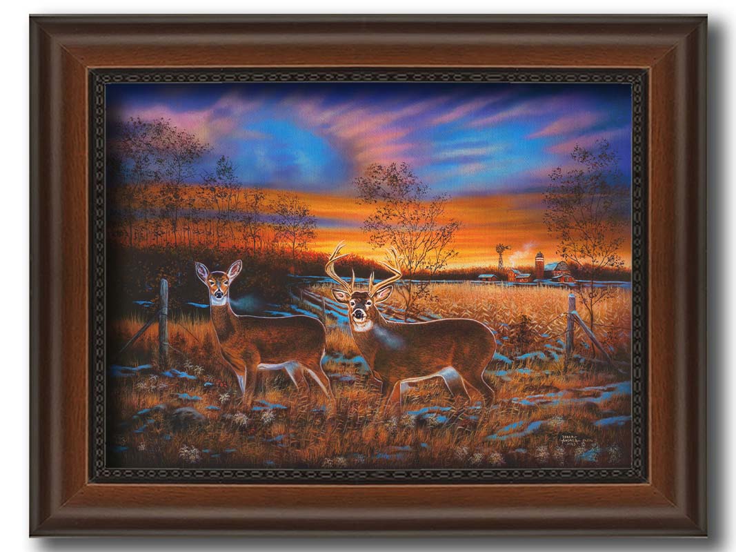 A painting of two whitetail deer in a field during a vivid sunset, with a large barn in the background. Printed on canvas and framed.