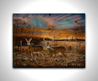 A painting of two whitetail deer in a field during a vivid sunset, with a large barn in the background. Printed on a wood pallet.