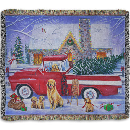 A throw blanket woven to design a painting of a vintage red truck carrying a Christmas tree to a decorated house, surrounded by a family of golden retriever dogs.