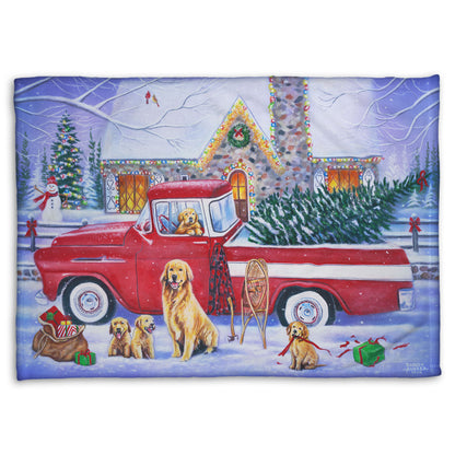 A coral fleece blanket printed with a painting of a vintage red truck carrying a Christmas tree to a decorated house, surrounded by a family of golden retriever dogs.