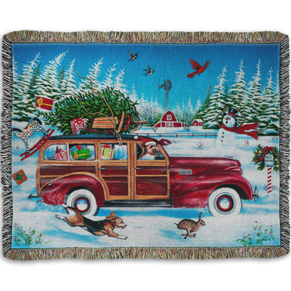 A woven throw blanket printed with a festive Christmas painting, with a classic wood panel car speeding by with presents.