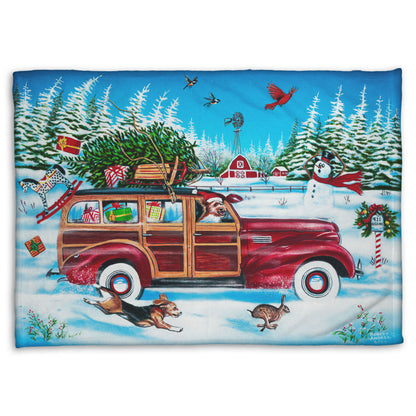 A coral fleece blanket printed with a festive Christmas painting, with a classic wood panel car speeding by with presents.