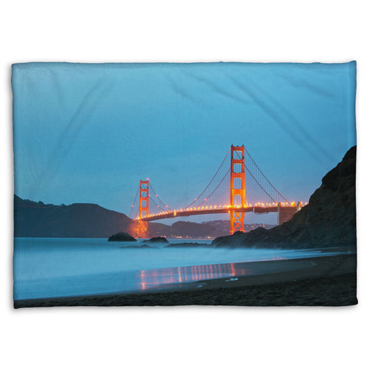 A coral fleece blanket designed with a photo from Baker Beach, San Francisco, looking out over the water at the Golden Gate Bridge.