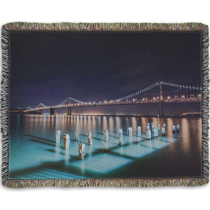 A woven throw blanket designed with a photo of the Oakland Bay Bridge in San Francisco at night, taken from the Embarcadero.