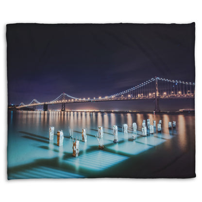 A coral fleece blanket designed with a photo of the Oakland Bay Bridge in San Francisco at night, taken from the Embarcadero.