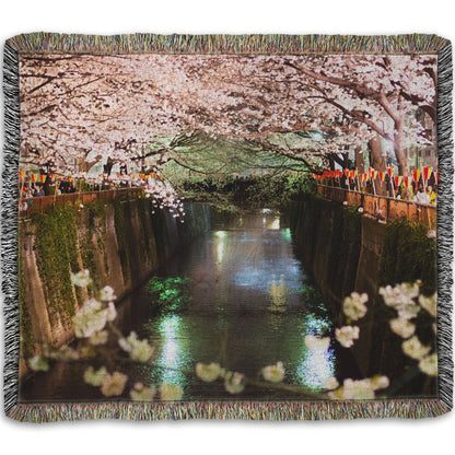 A woven throw blanket designed with a photo of cherry blossom trees over a canal at Meguro River in Tokyo, Japan.