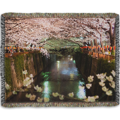 A woven throw blanket designed with a photo of cherry blossom trees over a canal at Meguro River in Tokyo, Japan.