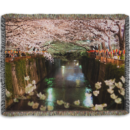 A woven throw blanket designed with a photo of cherry blossom trees over a canal at Meguro River in Tokyo, Japan.