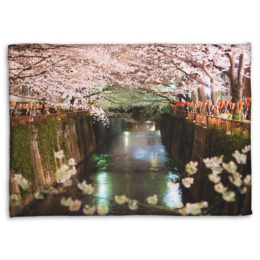 A coral fleece blanket designed with a photo of cherry blossom trees over a canal at Meguro River in Tokyo, Japan.