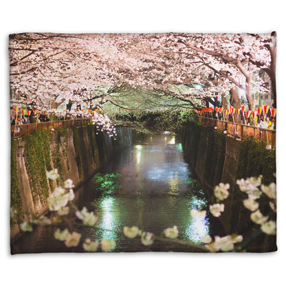 A coral fleece blanket designed with a photo of cherry blossom trees over a canal at Meguro River in Tokyo, Japan.