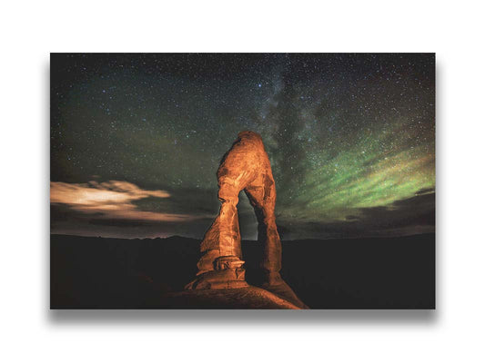 Nighttime photo of Delicate Arch in Arches National Park, Utah. The arch is lit with staged lighting, with a backdrop of a starry night sky. Printed on canvas.