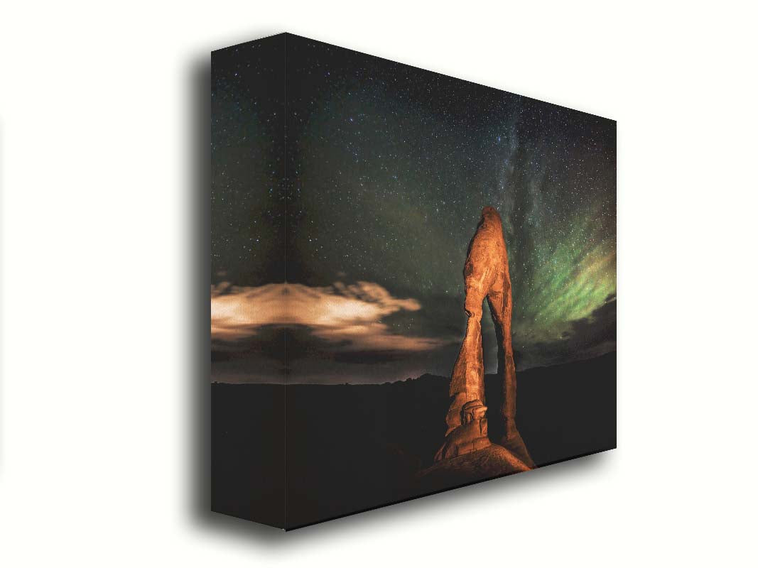 Nighttime photo of Delicate Arch in Arches National Park, Utah. The arch is lit with staged lighting, with a backdrop of a starry night sky. Printed on canvas.