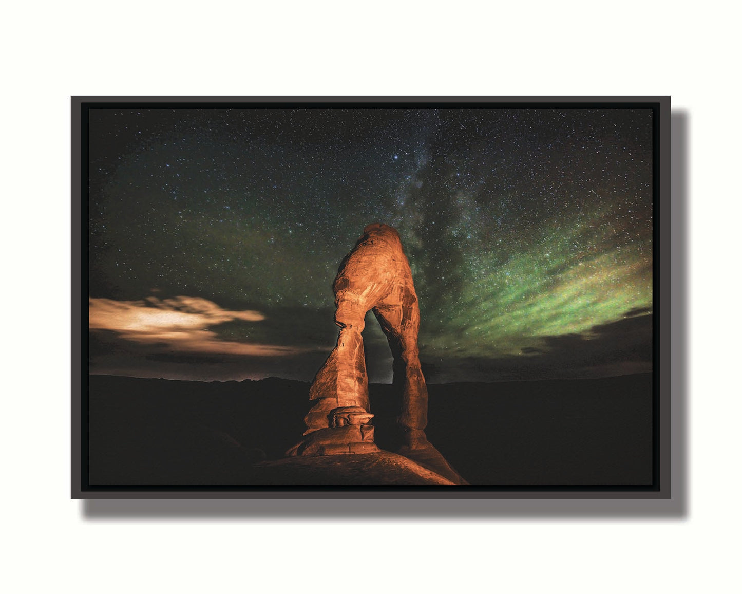 Nighttime photo of Delicate Arch in Arches National Park, Utah. The arch is lit with staged lighting, with a backdrop of a starry night sky. Printed on canvas in a float frame.