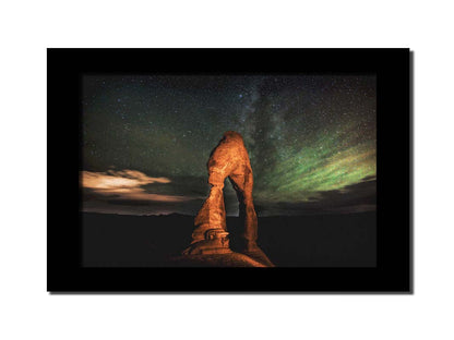 Nighttime photo of Delicate Arch in Arches National Park, Utah. The arch is lit with staged lighting, with a backdrop of a starry night sky. Printed on canvas and framed.